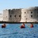 3 kayakers paddling through the water in front of the stone fortification of Dubrovnik